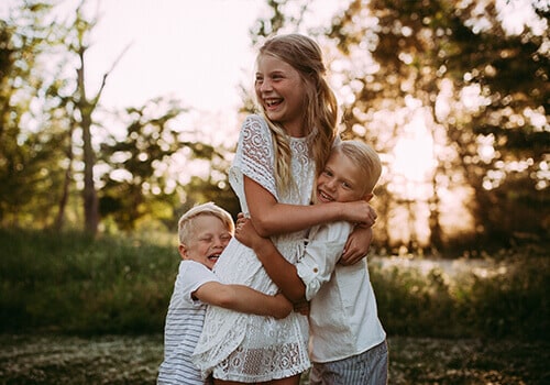 Dr. Minert's three children laughing and hugging in a field